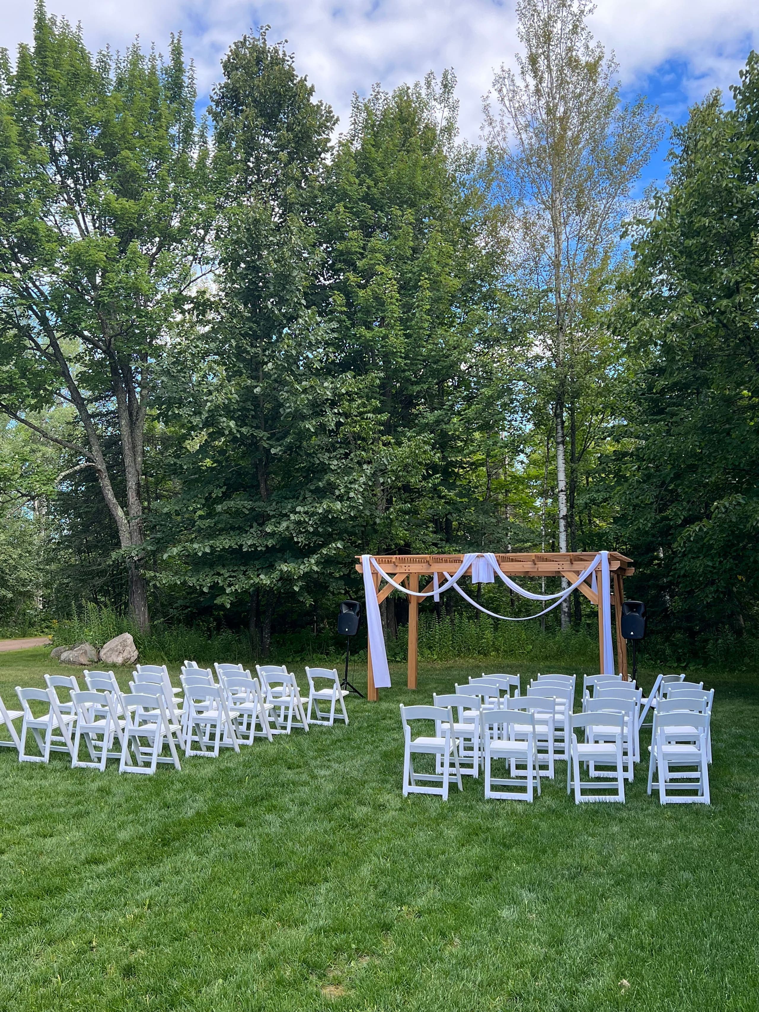 Outdoor wedding ceremony setup with white chairs and pergola